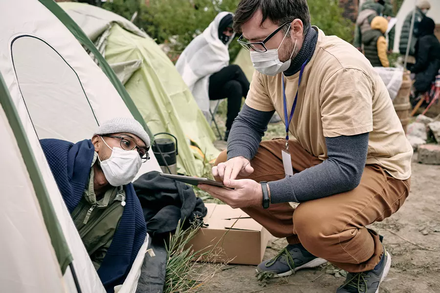 A healthcare worker checks on a masked elderly person at a campsite.
