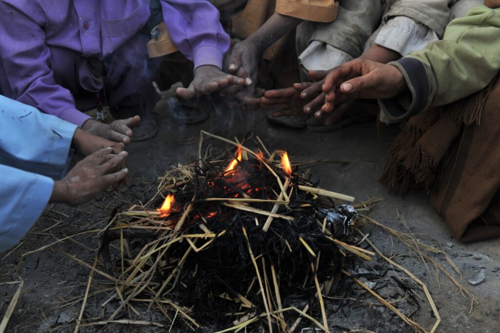 Group of people warming hands around a small fire.