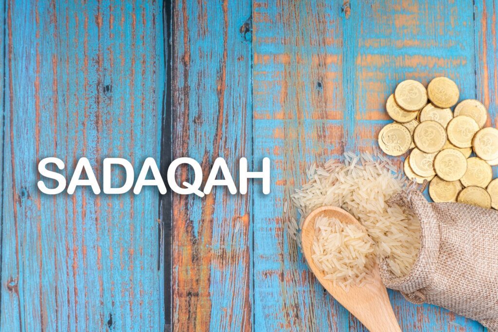 Coins and wheat on a wooden surface with the word 'Sadaqah'.