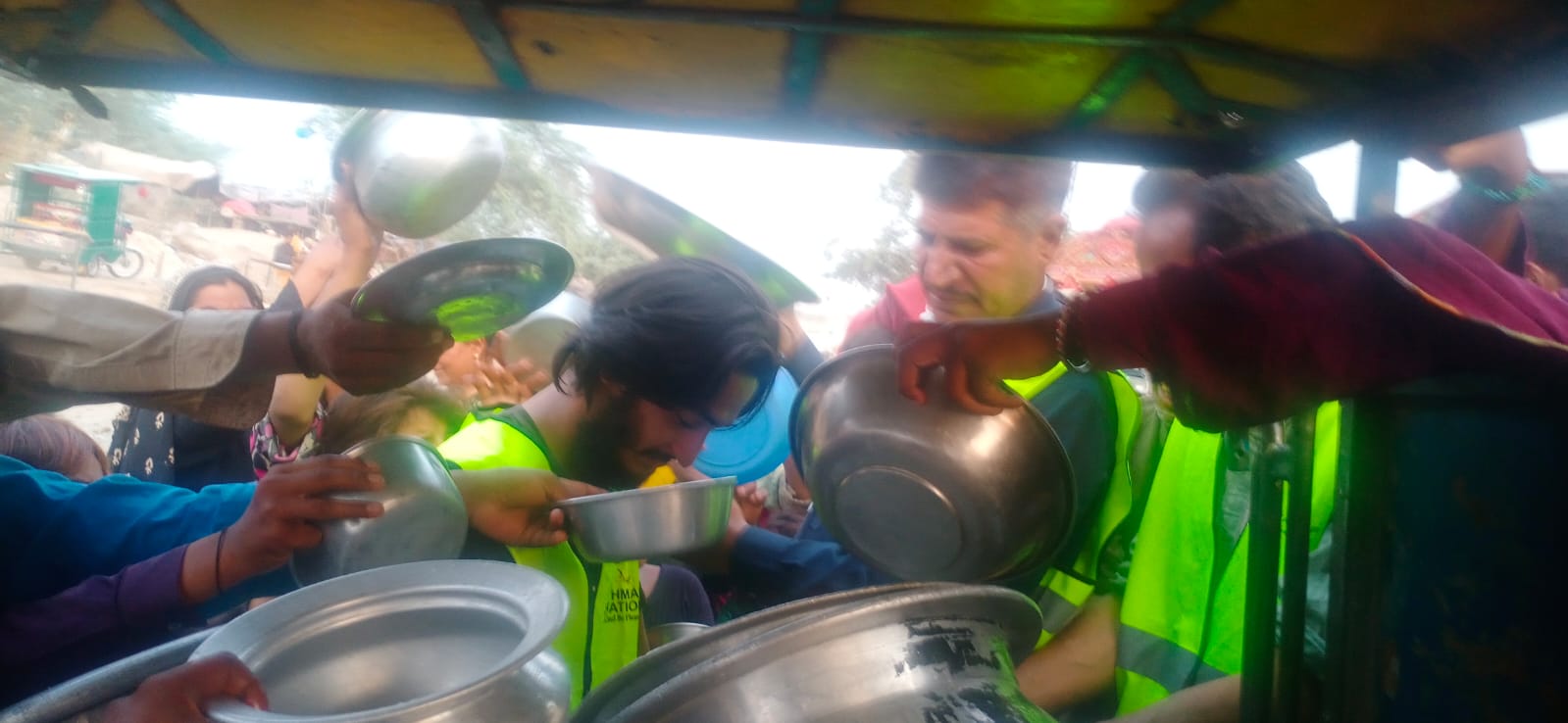 Crowd reaching metal bowls for food distribution